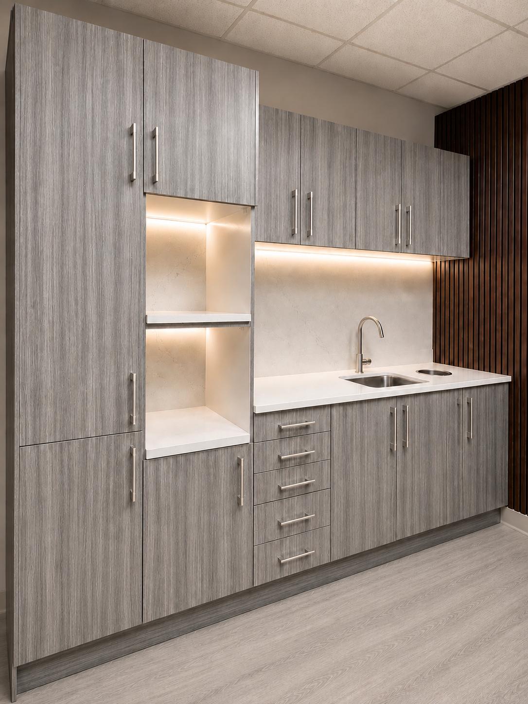 Light grey woodgrain dental sterilization center by DRM Dental with tall storage column, lit open shelving, quartz countertop, sink, and drawer bank
